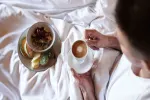 Eine Person hält eine Tasse Kaffee im Bett mit Frühstück.