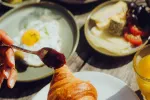 Hand mit Löffel, die Marmelade auf einem Frühstückstisch serviert