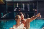 Paar genießt Zeit am Pool, lächelt und zeigt