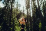 Person mit Yoga im Wald umgeben von hohen Bäumen